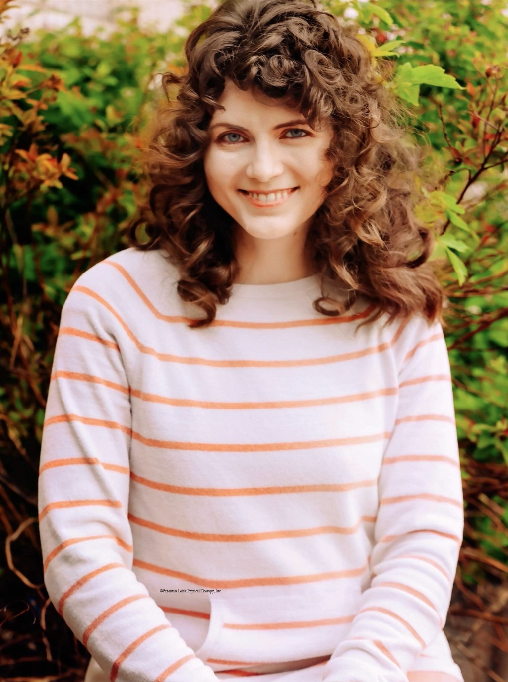 Melissa headshot-curly brown hair  wearing a white and thin orange striped hoodie